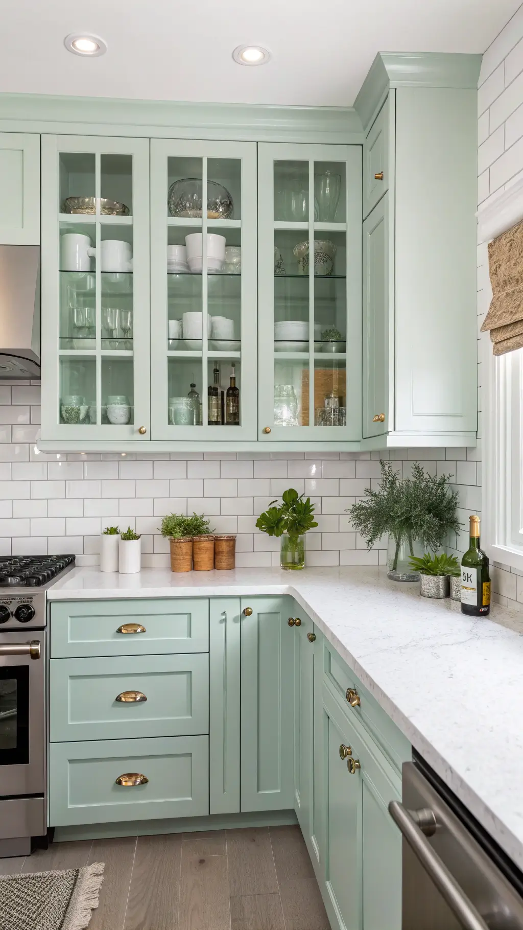Bright corner kitchen with seafoam green glass-front cabinets, white quartz counters with pottery and herbs, and stainless appliances under morning light
